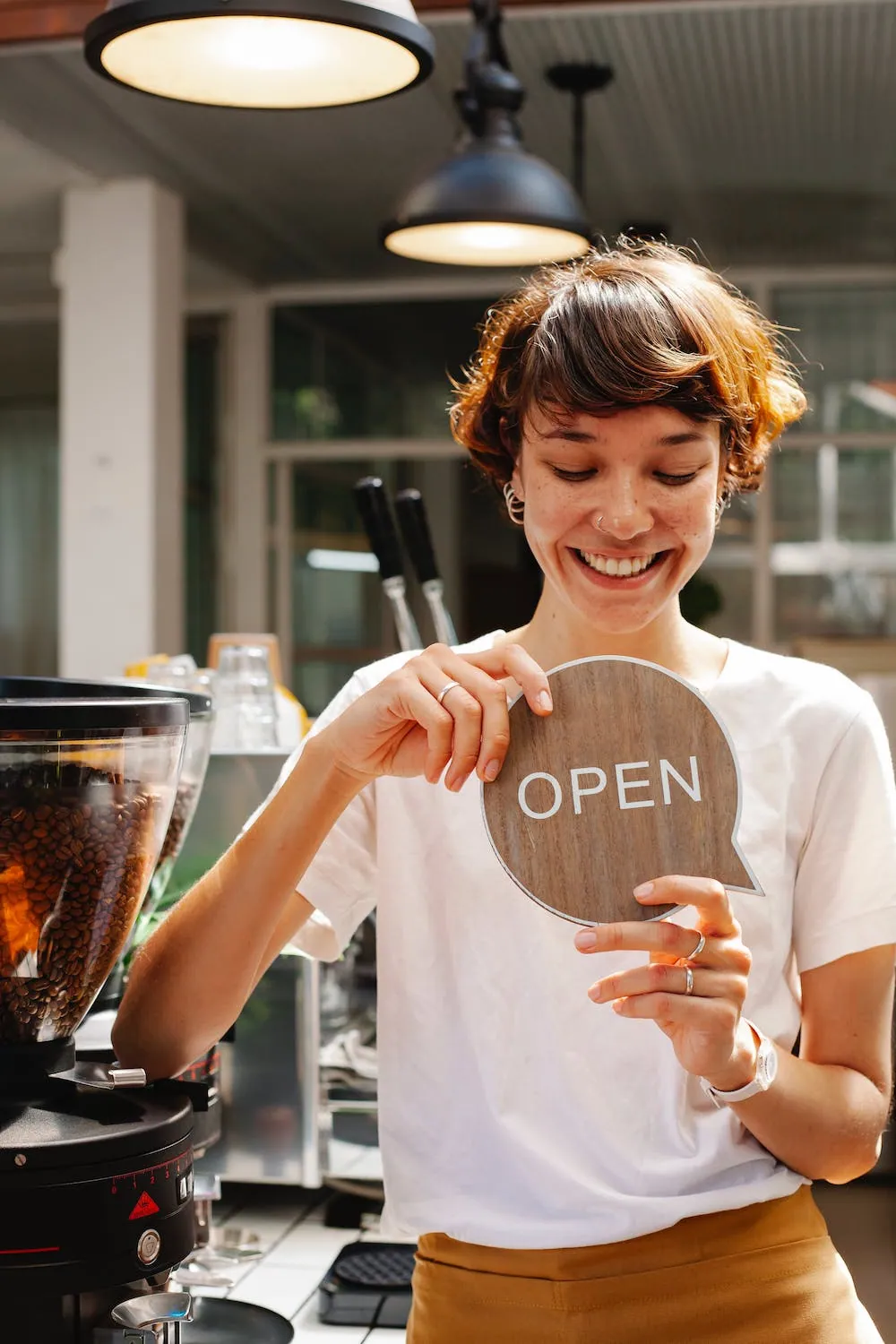 Coffee shop owner with open sign smiling